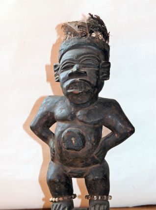 Statuette fétiche en bois avec plumes sur la tête et graines